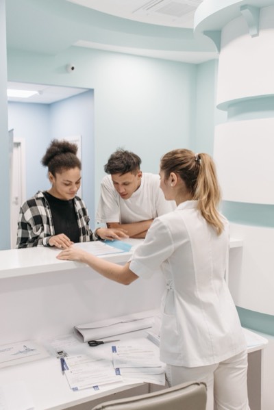 A receptionist helping two patients at a clinic desk