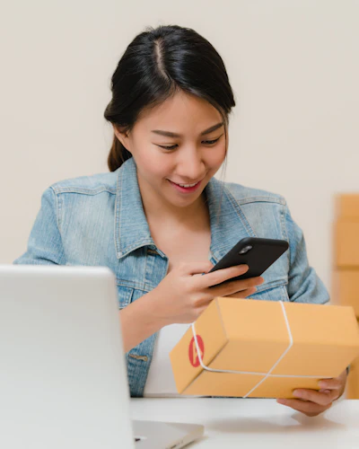 A founder checking an order on her phone beside a parcel